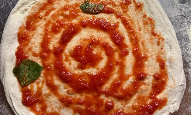 Hand-milled Italian tomato sauce spread onto fresh pizza dough